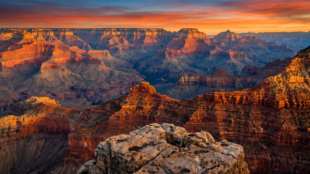 Wide panoramic sunset view of the Grand Canyon South Rim with layered orange and rust sandstone cliffs